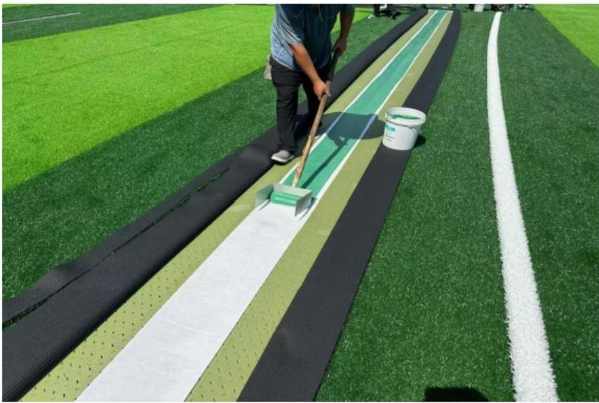 Applying two-component adhesive on seaming tape for artificial turf seams
