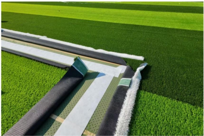 PET seaming tape positioned beneath the artificial turf joint